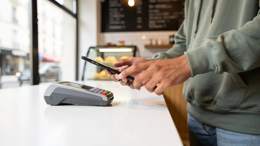Étudiant effectuant un paiement sans contact avec son smartphone sur un terminal de paiement dans un café